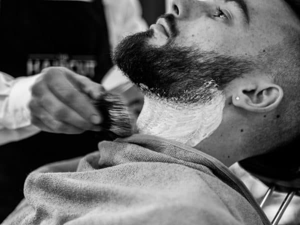 grayscale photo of man shaving his beard